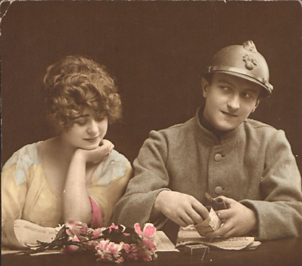 Colorized photograph of a soldier sitting alongside a woman. Flowers, a deck of cards, and papers sit on a table in front of them.