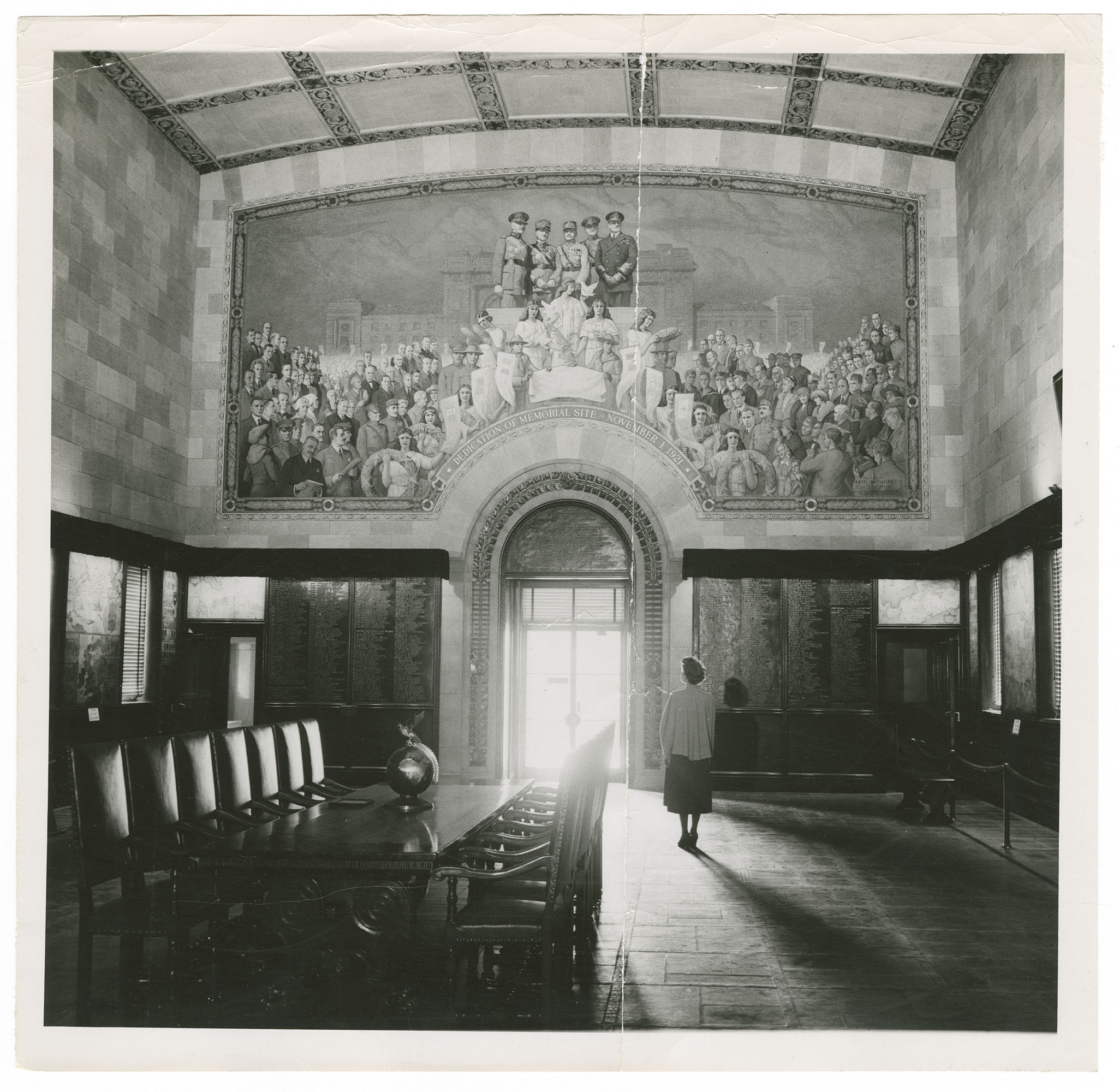 Black and white photo of the interior of Memory Hall, dominated by a painted mural of military figures on a dais surrounded by crowds.