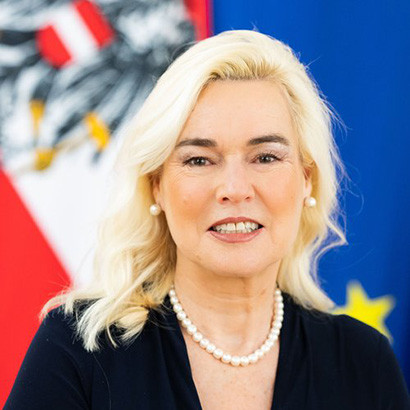 Portrait photograph of a white woman with white-blonde hair wearing a black suit jacket and pear necklace