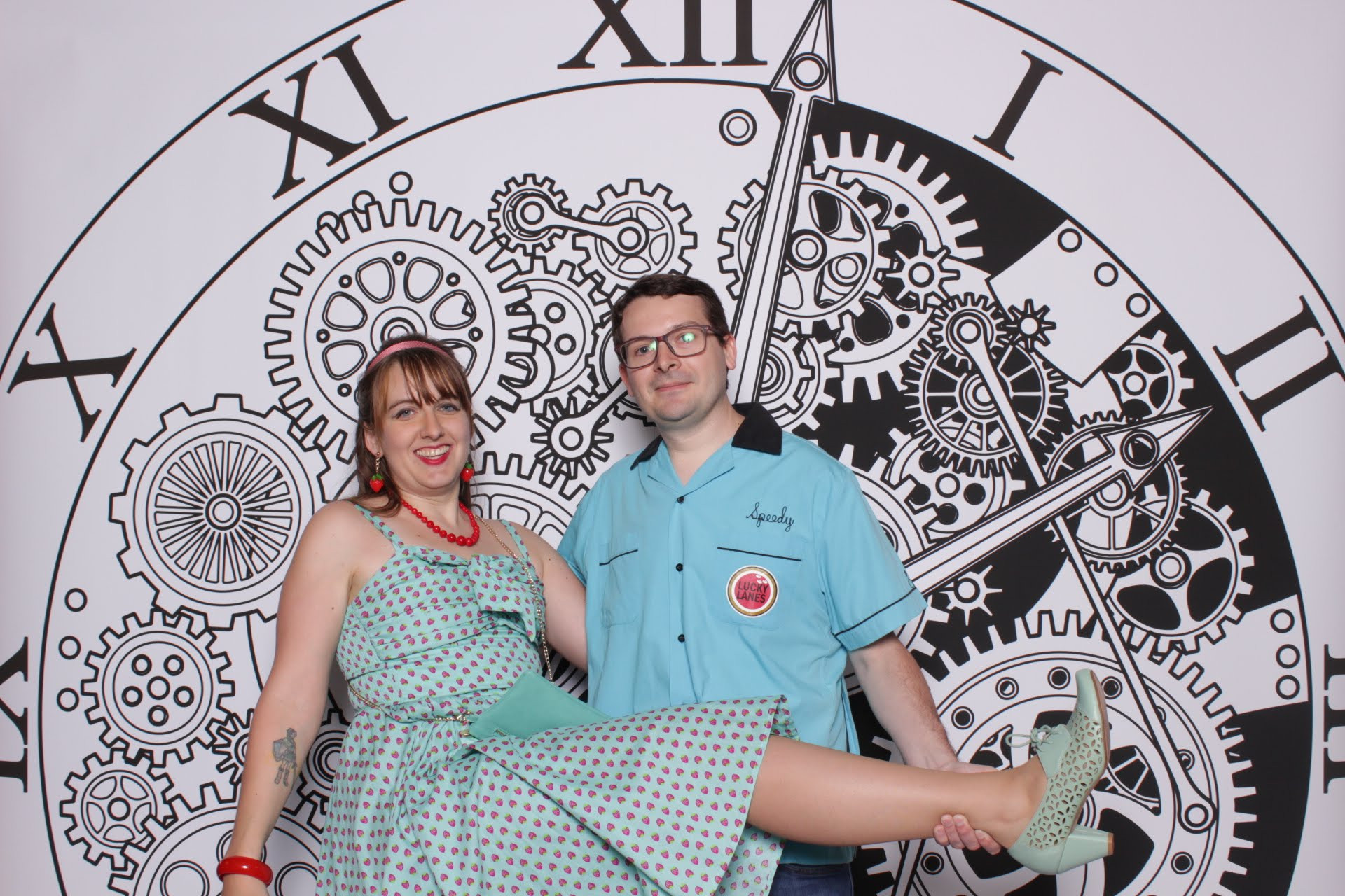 A woman dressed in a seafoam green 1950s-style cocktail dress poses exuberantly with a man dressed in a blue 1950s-style collared shirt